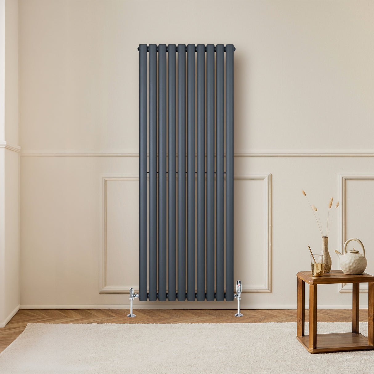 Ovale design radiator in antraciet grijs met haakse thermostaatkraan, geplaatst tegen een lichte wand in een moderne woonkamer