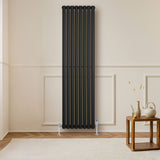 Ovale zwarte design radiator met één kolom, 1800 mm x 480 mm, geplaatst tegen een lichte muur, met een haakse thermostaatkraan