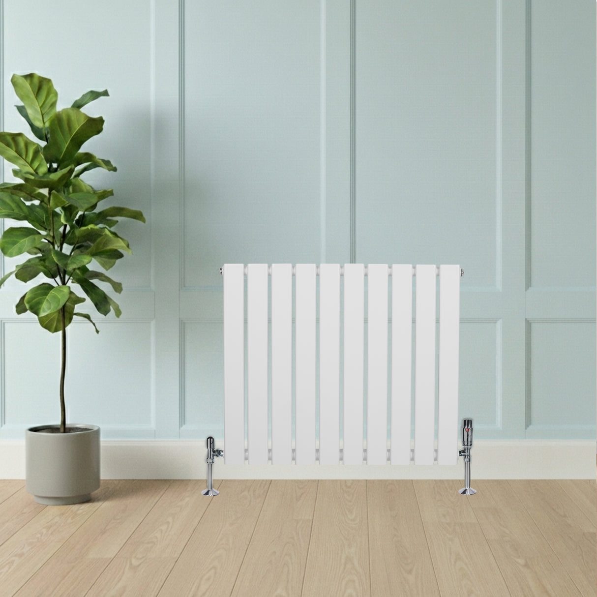 Witte designradiator met vlakke panelen en haakse thermostaatkraan, geplaatst tegen een lichte muur, met een groene plant ernaast