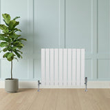 Witte designradiator met vlakke panelen en haakse thermostaatkraan, geplaatst tegen een lichte muur, met een groene plant ernaast