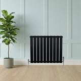 Zwart design radiator met vlakke panelen en haakse thermostaatkraan, geplaatst tegen een lichte muur met een groene plant ernaast