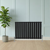 Zwart design radiator met vlakke panelen en haakse thermostaatkraan, geplaatst tegen een lichtblauwe wand met een groene plant ernaast