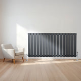 Vlakke panelen designradiator in antraciet grijs, 600 x 1190mm, met haakse thermostaatkraan, geplaatst naast een moderne stoel