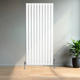 Witte design radiator met vlakke panelen en haakse thermostaatkraan, geplaatst tegen een muur in een moderne ruimte met houten vloer en planten