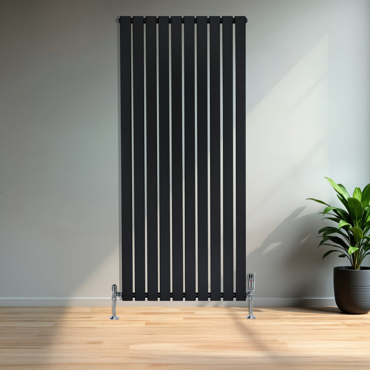 Zwarte designradiator met vlakke panelen en haakse thermostaatkraan, geplaatst tegen een lichte muur met een groene plant ernaast