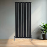 Zwarte designradiator met vlakke panelen en haakse thermostaatkraan, geplaatst tegen een lichte muur met een groene plant ernaast