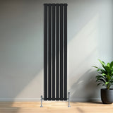 Zwarte designradiator met vlakke panelen en haakse thermostaatkraan, geplaatst tegen een lichte muur in een moderne ruimte