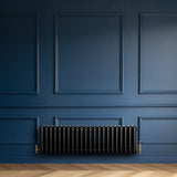 Zwarte traditionele 4-kolom radiator van 300 x 1010 mm met haakse thermostaatkraan, geplaatst tegen een diepblauwe muur