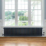 Traditionele antraciet grijze 4-kolom radiator van 300 x 1370 mm met haakse thermostaatkraan, geplaatst onder een groot raam