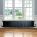 Traditionele antraciet grijze 4-kolom radiator van 300 x 1505 mm met haakse thermostaatkraan, geplaatst onder een raam