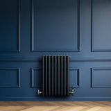 Traditionele antraciet grijze 4-kolom radiator met haakse thermostaatkraan, geplaatst tegen een diepblauwe wand