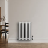 Traditionele witte 4-kolom radiator van 600 x 425 mm met haakse thermostaatkraan, geplaatst tegen een lichte muur in een moderne ruimte
