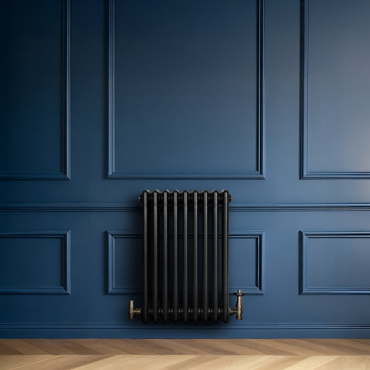 Zwarte traditionele 4-kolom radiator van 600 x 425 mm met haakse thermostaatkraan, geplaatst tegen een diepblauwe wand