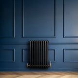 Zwarte traditionele 4-kolom radiator van 600 x 425 mm met haakse thermostaatkraan, geplaatst tegen een diepblauwe wand