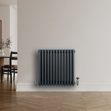 Traditionele antraciet grijze 4-kolom radiator met haakse thermostaatkraan, geplaatst tegen een lichte muur in een moderne ruimte