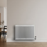 Witte traditionele 4-kolom radiator van 600 x 785 mm met een haakse thermostaatkraan, geplaatst tegen een lichte muur