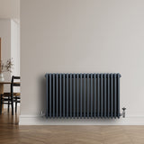 Traditionele antraciet grijze 4-kolom radiator van 600 x 1010 mm met haakse thermostaatkraan, geplaatst tegen een lichte muur