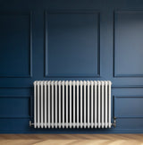 Traditionele witte 4-kolom radiator van 600 x 1010 mm met haakse thermostaatkraan, geplaatst tegen een donkerblauwe muur