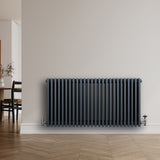 Traditionele antraciet grijze 4-kolom radiator van 600 x 1190 mm met haakse thermostaatkraan, geplaatst tegen een lichte muur