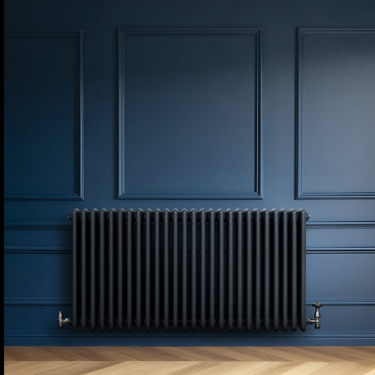 Traditionele 4-kolom radiator in antracietgrijs, met een strakke, verticale vorm en haakse thermostaatkraan, tegen een blauwe muur