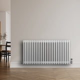 Witte traditionele 4-kolom radiator van 600 x 1190 mm met haakse thermostaatkraan, geplaatst tegen een lichte muur in een moderne ruimte