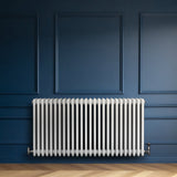 Traditionele witte 4-kolom radiator van 600 x 1190 mm tegen een donkerblauwe muur, met een haakse thermostaatkraan aan de zijkant