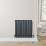 Ovale antraciet grijze designradiator met één kolom, inclusief haakse thermostaatkraan, tegen een lichte muur geplaatst