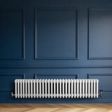 Traditionele witte 4-kolom radiator van 300 x 1370 mm tegen een diepblauwe wand, met een glanzende afwerking en ronde vormen