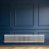 Traditionele witte 4-kolom radiator van 300 x 1505 mm, geplaatst tegen een donkerblauwe muur met een houten vloer eronder