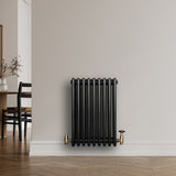 Traditionele zwarte 4-kolom radiator van 600 x 425 mm met glanzende afwerking en gouden kranen, geplaatst tegen een lichte muur