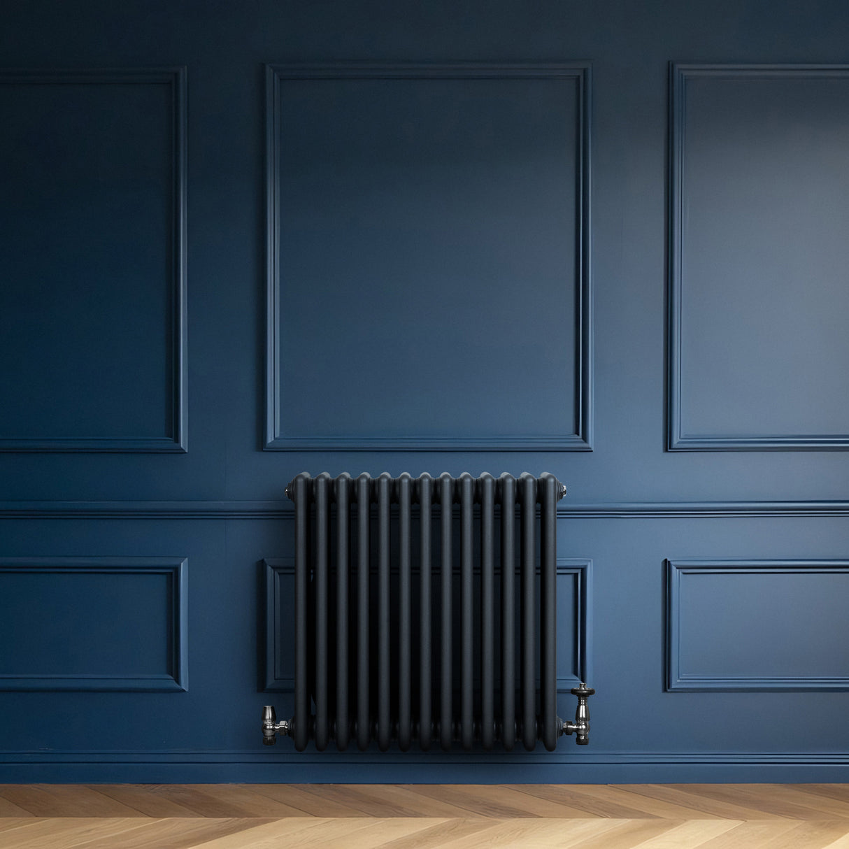 Traditionele antraciet grijze 4-kolom radiator van 600 x 605 mm tegen een diepblauwe wand, met een strakke, moderne uitstraling