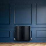 Traditionele antraciet grijze 4-kolom radiator van 600 x 605 mm tegen een diepblauwe wand, met een strakke, moderne uitstraling