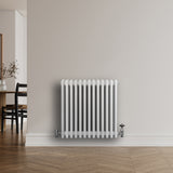 Traditionele witte 4-kolom radiator van 600 x 605 mm met glanzende afwerking, geplaatst tegen een lichte muur in een moderne ruimte