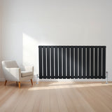 Zwarte design radiator met vlakke panelen, 1 kolom, 600 x 1190mm, geplaatst tegen een lichte muur naast een moderne stoel