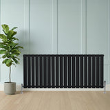 Zwart designradiator met vlakke panelen en één kolom, geplaatst tegen een lichte wand, naast een groene plant in een pot
