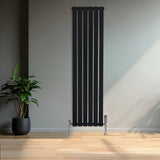 Zwarte designradiator met vlakke panelen en één kolom, 1600 x 420mm, geplaatst tegen een lichte muur met een groene plant ernaast