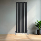 Zwarte designradiator met vlakke panelen en één kolom, 1600 x 560 mm, geplaatst tegen een lichte muur met een groene plant ernaast