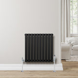 Ovale zwarte designradiator met één kolom, 600 mm x 600 mm, geplaatst tegen een lichte muur in een moderne woonkamer