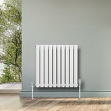 Ovale witte designradiator met één kolom, 600 mm x 600 mm, geplaatst tegen een groene muur in een lichte ruimte met houten vloer