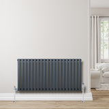 Ovale design radiator in antraciet grijs, 1 kolom, 600 mm x 1200 mm, met glanzende bevestigingen op een lichte muur en houten vloer