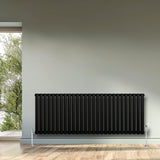 Ovale zwarte design radiator met één kolom, 600 mm x 1620 mm, geplaatst tegen een lichte muur met een houten vloer en raam uitzicht op groen
