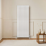 Ovale witte designradiator met één kolom, 1600 mm x 600 mm, geplaatst tegen een lichte muur met houten vloer en een houten tafel