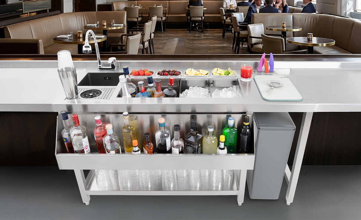Een moderne bar met een metalen werkblad, gevuld met flessen, ijs, fruit en glazen, in een stijlvolle restaurantomgeving