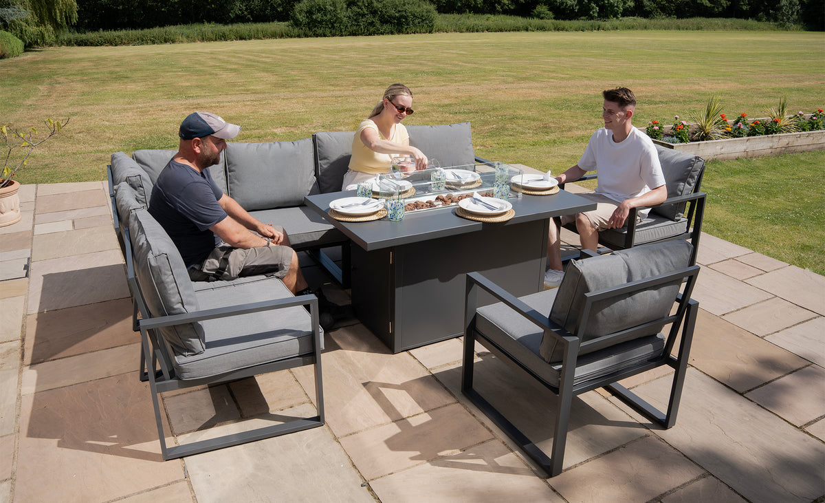 Moderne tuinset met grijze kussens, een grote tafel en drie mensen die genieten van een maaltijd op een zonnige dag in de tuin