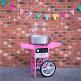 Roze suikerspinmachine met een glanzende metalen kom, geplaatst tegen een bakstenen muur met kleurrijke vlaggetjes erboven