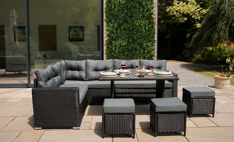 Luxe tuinset met een grijze kussenbank, een tafel en bijzetstoelen, omringd door groene planten en een moderne achtergrond