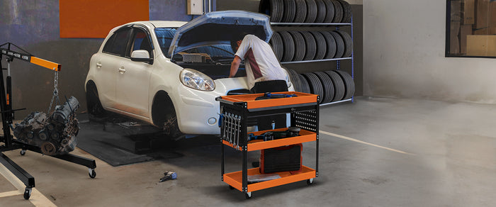 Een monteur werkt aan de motorkap van een witte auto, met een oranje gereedschapswagen vol gereedschap op de voorgrond
